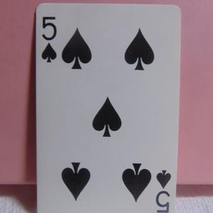 May include: A standard playing card with a white background and black spades. The card is a five of spades.