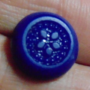 May include: A dark blue glass button with a white floral design in the center.