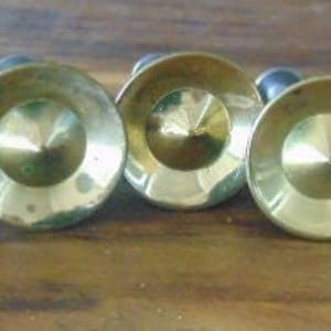 May include: Five gold-toned metal drawer pulls with a pointed center and a slightly raised rim. The pulls are attached to a black screw.