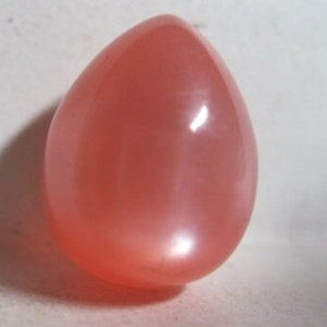 May include: A smooth, teardrop-shaped, pink gemstone with a pearlescent sheen.