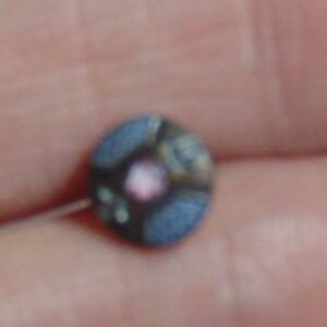May include: A small, round, multi-colored button with a pink center. The button has a blue, brown, and white pattern.