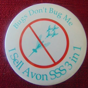 May include: White round button with a red circle and a diagonal line through it. The circle has a blue image of a mosquito with wings. The text around the circle says "Bugs Don't Bug Me". The text below the circle says "I Sell Avon SSS 3 in 1".