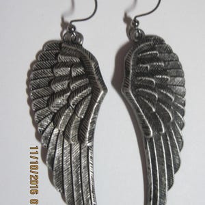 May include: A pair of silver-toned metal earrings shaped like detailed bird wings with textured feather patterns. Each wing hangs from a curved ear wire. The text 11/10/2016 01:16 is visible on the left side of the image, printed in yellow.