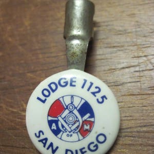May include: A white enamel pin with a blue and red Masonic symbol and the text "LODGE 1125 SAN DIEGO OF A.M."