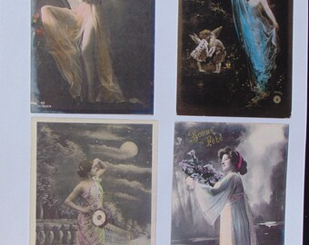 May include: Four vintage postcards featuring women in various poses. The first postcard shows a woman in a flowing white dress with a moon in the background. The second postcard shows a woman in a blue dress with a fairy and a man in the background. The third postcard shows a woman in a white dress with a bouquet of flowers. The fourth postcard shows a woman in a pink and green dress with a moon in the background.