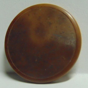 May include: A round, brown object with a slightly textured surface and a raised edge. The object appears to be made of a solid material, possibly plastic or a similar substance. The color is a warm, medium brown.
