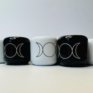 May include: Five ceramic containers in a row, alternating between black and white. Each has a triple moon phase design in white. The containers are cylindrical with rounded edges, and sit on a white surface.