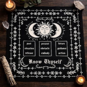 May include: Black tarot cloth with white celestial design. Features a sun and moon motif, with text boxes for past, present, and future readings. The words "Know Thyself" are at the bottom. Includes candles and crystals.