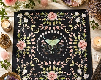 May include: Black square textile with a floral and celestial design. Features pink roses, crescent moons, and a central moth illustration. The border has a repeating floral pattern with pink and white flowers.