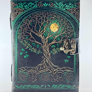 May include: A black leather journal with a tree of life design. The cover features a detailed illustration of a tree with a full moon, in shades of gold and green. The journal has a clasp closure.