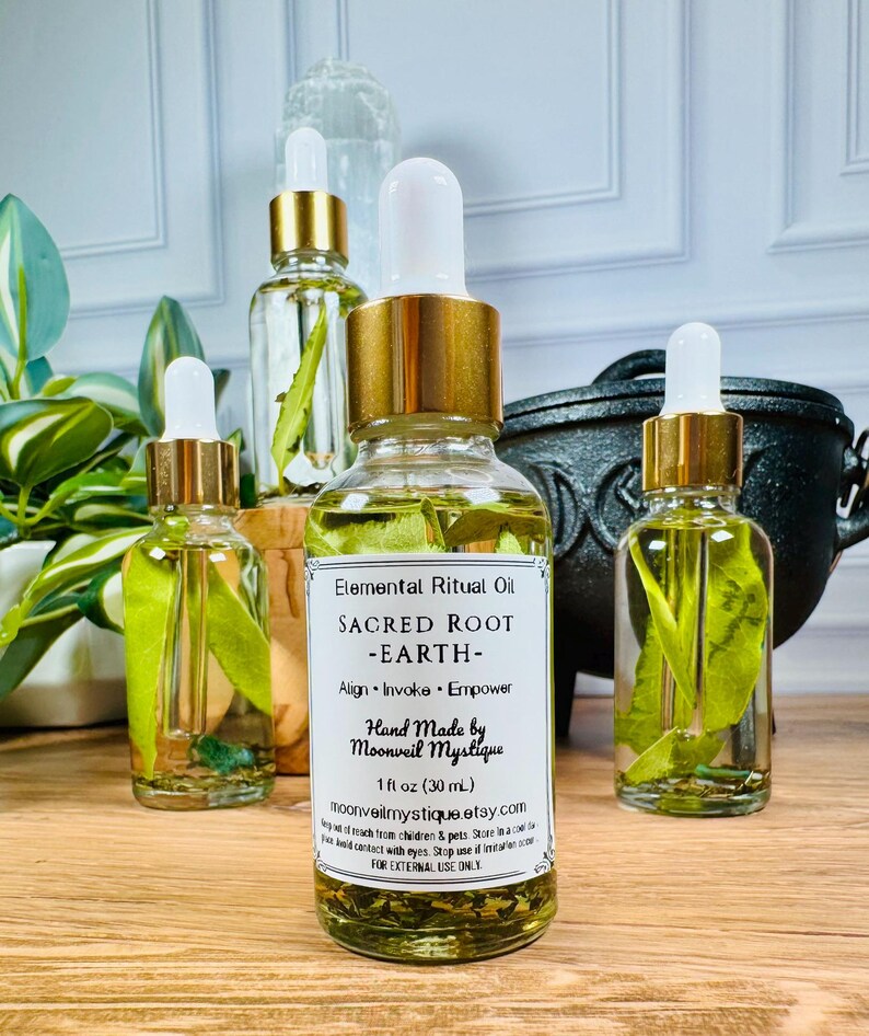 May include: Three clear glass dropper bottles filled with yellow oil and green leaves. The central label reads Elemental Ritual Oil, SACRED ROOT -EARTH-, Align, Invoke, Empower, Hand Made by Moonveil Mystique, 1 fl oz (30 mL), moonveilmystique.etsy.com.