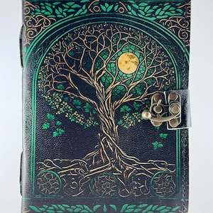 May include: Black leather journal with a tree of life design. The cover features a detailed illustration of a tree with a full moon, in shades of green and gold. It has a metal clasp and a leather strap closure.