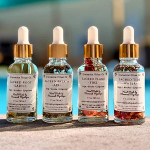 May include: Four clear glass dropper bottles, each containing 30 ml of oil with botanical inclusions. Labels read Elemental Ritual Oil, Sacred Root-Earth, Sacred Breath-Air, Sacred Flame-Fire, and Sacred Tide-Water, with gold-toned dropper caps.