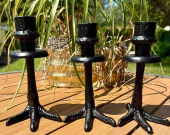 以下が含まれることがあります： 3つの黒いキャンドルホルダー。それぞれが3本の指を持つ鳥の足の形をしたテクスチャーのあるベースを備えています。垂直のステムは円形のプラットフォームと円筒形の上部に続き、テーパーキャンドルをしっかりと保持するように設計されています。