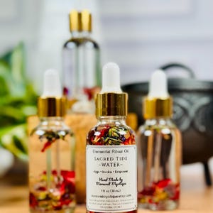 May include: Three clear glass dropper bottles filled with clear oil and dried flower petals. Each bottle has a gold collar and white dropper top. The front label reads: Elemental Ritual Oil, SACRED TIDE ~WATER~, Align &middot; Invoke &middot; Empower, Hand Made by Moonveil Mystique, 1 fl oz (30 mL).