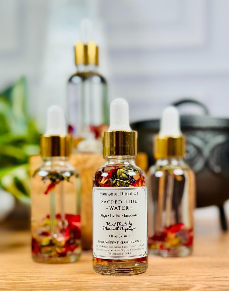 May include: Three clear glass dropper bottles filled with clear oil and dried flower petals. Each bottle has a gold collar and white dropper top. The front label reads: Elemental Ritual Oil, SACRED TIDE ~WATER~, Align &middot; Invoke &middot; Empower, Hand Made by Moonveil Mystique, 1 fl oz (30 mL).