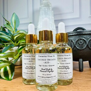 May include: Three clear glass dropper bottles containing light yellow liquid, each with a white label reading Elemental Ritual Oil, SACRED BREATH, AIR, Align, Invoke, Empower, Hand Made by Moonveil Mystique, and 1 fl oz (30 mL).