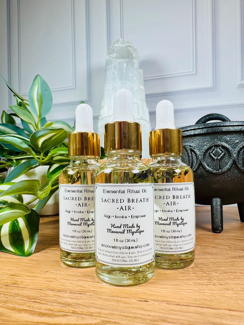 May include: Three clear glass dropper bottles containing light yellow liquid, each with a white label reading Elemental Ritual Oil, SACRED BREATH, AIR, Align, Invoke, Empower, Hand Made by Moonveil Mystique, and 1 fl oz (30 mL).