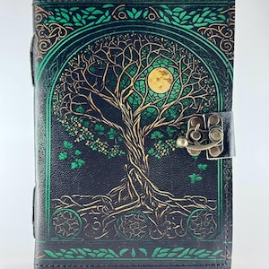 May include: A black leather journal with a detailed tree of life design in green and gold. The cover features a full moon and intricate branches. The journal has a metal clasp closure and green border accents.