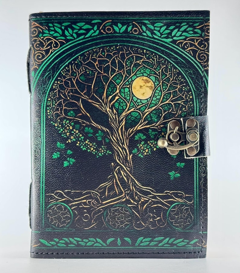 May include: A black leather journal with a detailed tree of life design in green and gold. The cover features a full moon and intricate branches. The journal has a metal clasp closure and green border accents.