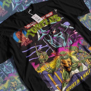 Può includere: T-shirt nera con grafica in stile fumetto dei Teenage Mutant Ninja Turtles. Il design include le parole "Teenage Mutant Ninja Turtles" e "Heroes in a Half Shell". La maglietta ha un'etichetta con la scritta "Large".