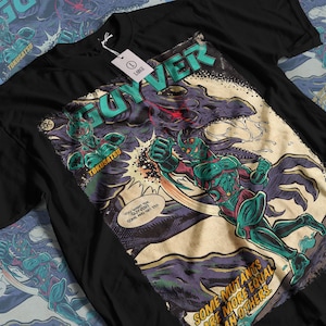 Puede incluir: Camiseta negra con un diseño gráfico de estilo cómic. El diseño presenta la palabra "GUYVER" en verde azulado, una figura blindada verde y roja y un monstruo morado. El texto incluye "TOKUSATSU" y "ALGUNOS MUTANTES SON MÁS IGUALES QUE OTROS."