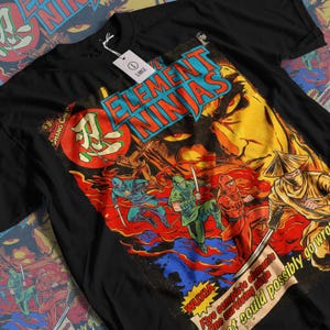 Könnte beinhalten: Schwarzes T-Shirt mit einem Comic-Grafik-Design mit der Aufschrift "ELEMENT NINJAS". Das Design zeigt Ninja-Illustrationen und ein großes Gesicht im Hintergrund. Das T-Shirt hat ein Etikett mit der Aufschrift "LARGE".