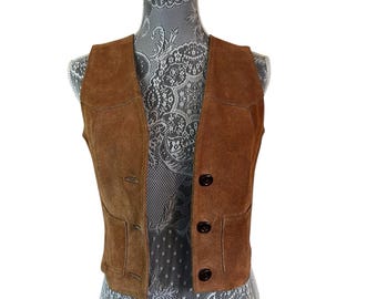 May include: A brown suede vest with a V-neck and three dark brown buttons. The vest has two front pockets and is displayed on a mannequin. The vest is a classic style.