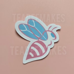 May include: A die-cut sticker featuring a stylized bee design. The bee has a white body with pink stripes and blue wings. The sticker is on a pink background.