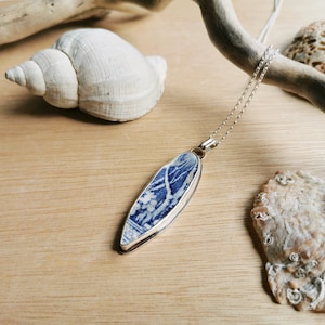 May include: A silver chain necklace with a blue and white porcelain pendant shaped like a surfboard. The pendant has a floral design.