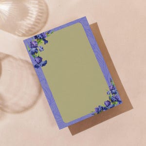 Pode incluir: Um conjunto de papelaria com uma folha de escrita com borda de lavanda com detalhes florais de íris em aquarela nos cantos. A folha de escrita tem um interior verde-oliva claro e repousa sobre um envelope marrom. O fundo é bege claro.