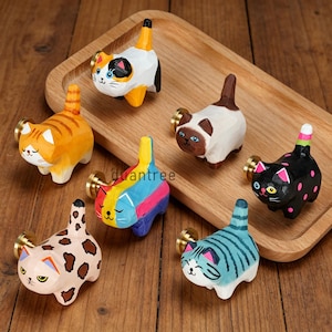 Puede incluir: Seis pomos para cajones con forma de gato hechos de madera tallada con detalles pintados. La colección incluye un gato calicó, un atigrado naranja, un siamés marrón y blanco, un gato negro con lunares rosas, uno multicolor y uno beige.