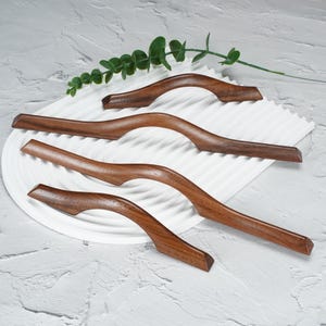 May include: Four dark brown wooden cabinet handles with a smooth, curved, wave-like design. Each handle features a polished finish that highlights the natural wood grain, arranged in a cascading pattern from shortest to longest.