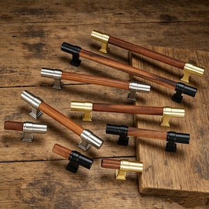 Könnte beinhalten: Eine Sammlung von Holzschrankgriffen mit Metallakzenten. Die Griffe haben eine dunkle Holzmaserung in der Mitte mit silbernen, goldenen und schwarzen Metallendkappen und Befestigungsteilen. Sie sind auf einer Holzoberfläche angeordnet.