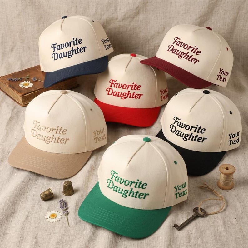 May include: A collection of baseball caps in various colors, including navy, red, green, and black. Each cap features the embroidered text "Favorite Daughter" and "Your Text" on the side. The caps are displayed on a neutral fabric.