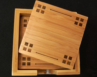 May include: A bamboo coaster set with a square design. The set includes a wooden box and four coasters. Each coaster and the box lid feature a decorative square pattern. The natural wood grain is visible.