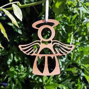 May include: A wooden angel ornament with a halo, wings, and a heart-shaped body. The ornament is painted in a light brown colour and has a string for hanging.