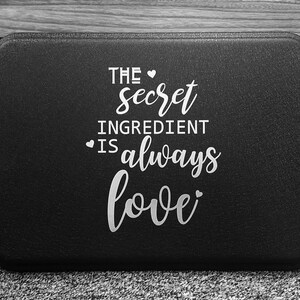May include: Black baking pan with white text that reads "The secret ingredient is always love".