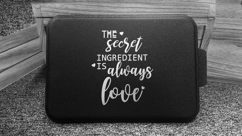 May include: Black baking pan with white text that reads "The secret ingredient is always love".