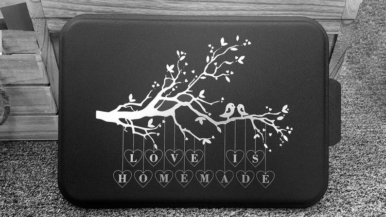 May include: Black and white graphic design of a tree with two birds perched on a branch. Hanging from the branches are hearts with the words "LOVE IS HOMEMADE" written on them.