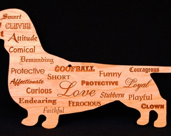 May include: A wooden dachshund-shaped sign with engraved words like "Love", "Funny", and "Loyal". The sign is light brown and has a black background. The words describe the dog's personality.