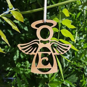 May include: A wooden angel ornament with a halo and wings. The angel is holding a letter "E" in its centre.