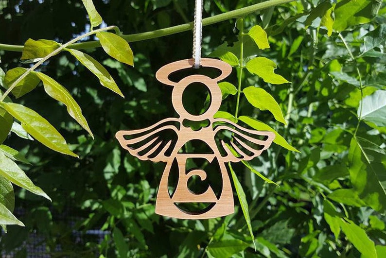 May include: A wooden angel ornament with a halo and wings. The angel is holding a letter "E" in its centre.