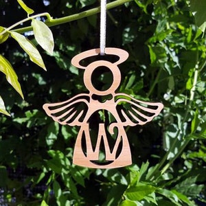 May include: Wooden angel ornament with a halo and wings, featuring a cutout letter "W" in the centre. The ornament is light brown and is hanging from a string.