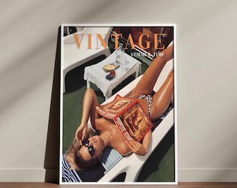 May include: A framed print with a vintage magazine cover design. The words "VINTAGE" and "SUMMER TIME" are visible. The image depicts a person sunbathing on a sun lounger, reading a magazine. A small table with items is in the background.
