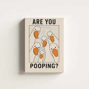 Op de afbeelding: Een canvas print met een humoristische illustratie van cartoon ganzen. De ganzen hebben witte veren en oranje snavels en kijken in een badkamer. De tekst "ARE YOU POOPING?" staat in het zwart afgedrukt.