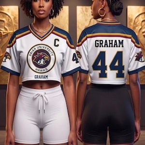 May include: Two women wearing matching white and navy athletic jerseys with the text "Briar University Hawks" and "Graham 44". The jerseys have gold accents and a hawk logo. One woman wears white shorts, the other wears black shorts.