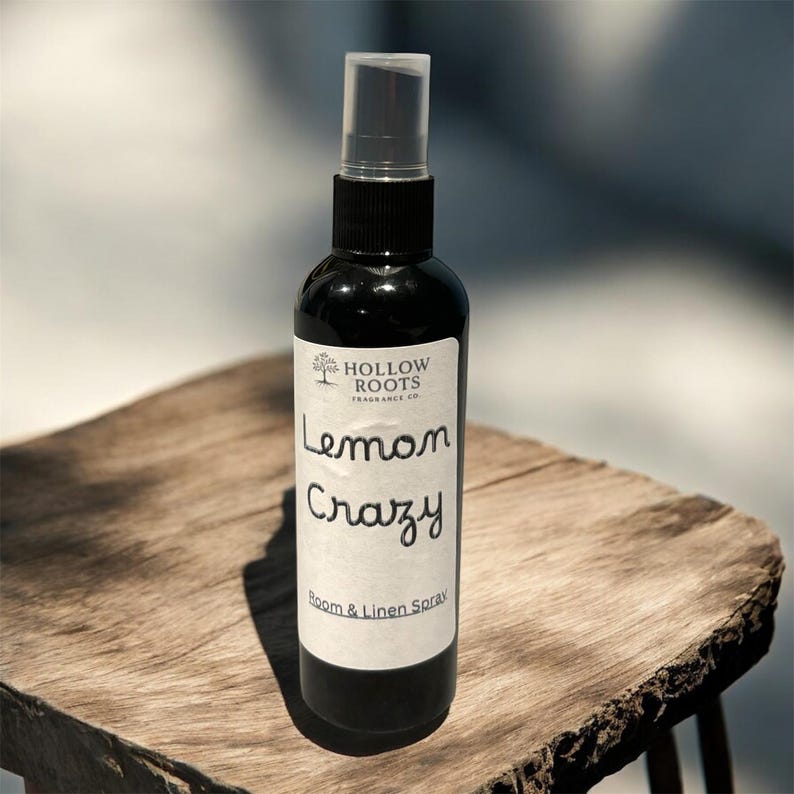 May include: A black room and linen spray bottle with a clear cap. The label reads "Lemon Crazy" and "Room & Linen Spray" in a handwritten style font. The bottle is on a wooden surface.