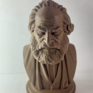 May include: A brown bust sculpture of a man with a long beard and hair, wearing a suit. The sculpture has a detailed face with closed eyes and is set on a round base. The bust is made of a solid material.