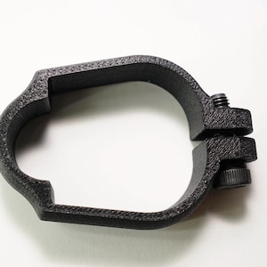 May include: A black, circular clamp with a textured finish. The clamp features a split design and a screw mechanism for adjustment. The product is designed to secure objects and is set against a white background.